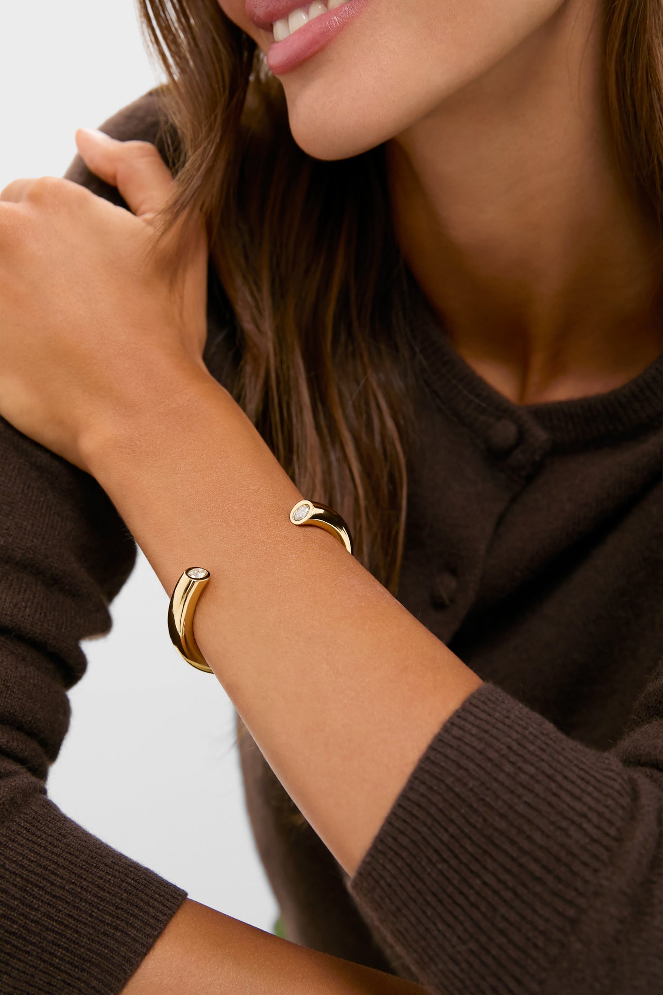 Woman wearing a classic dark brown knit sweater, showcasing the high-end Gold Miley Cuff on her wrist, featuring polished gold with gemstone accents, embodying effortless style and fun sophistication.