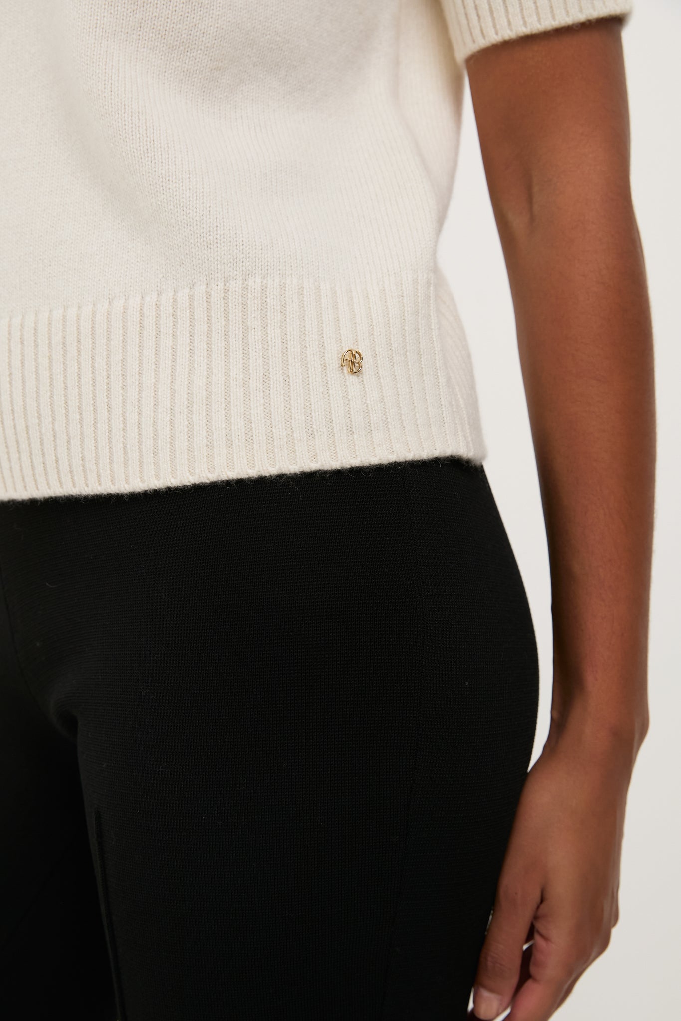 Close-up of the Ivory Jackson Sweater, a classic, effortless knit with ribbed hem and gold pin, paired with fitted black pants for a high-end, fun look.