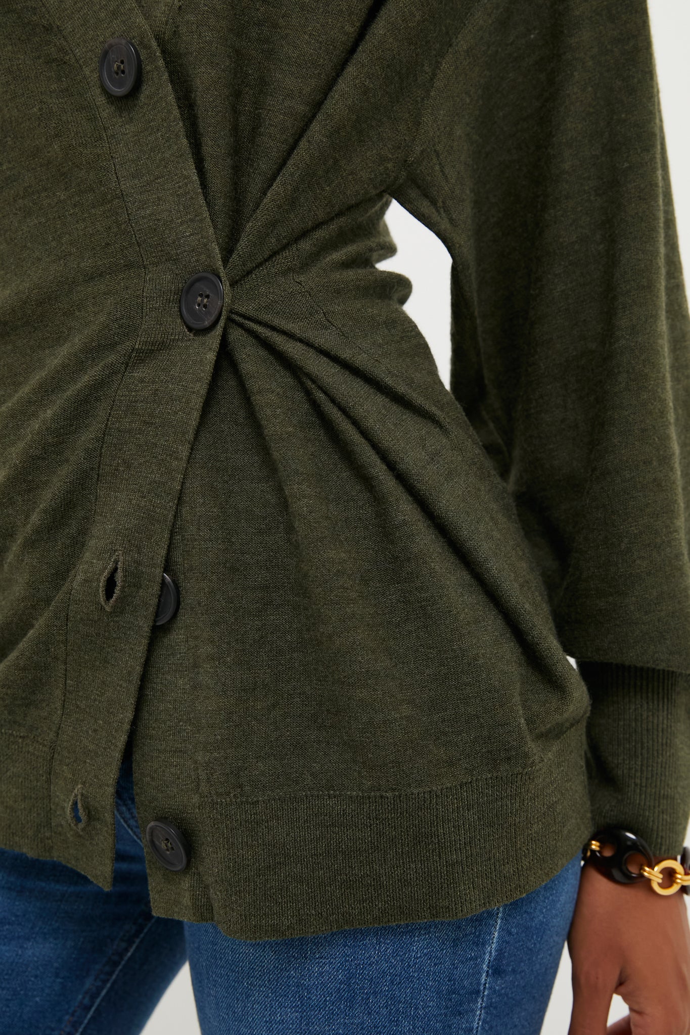 Person wearing the Olive Drippy Tissue Cardigan, featuring an effortless draped effect and asymmetrical fit, paired with jeans and a chunky bracelet for a classic, high-end look.