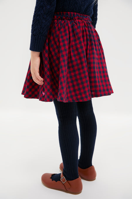 Child wearing the classic Red Blue Check Gianna Skirt with ruffle trim, paired effortlessly with navy tights and Mary Jane shoes, exuding a fun, high-end style.