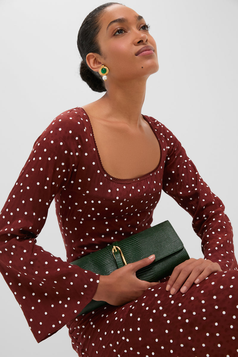 Woman in a classic Burnt Umber Narah Maxi Dress with polka dots, holding an emerald clutch, embodies effortless elegance and fun, capturing high-end style.