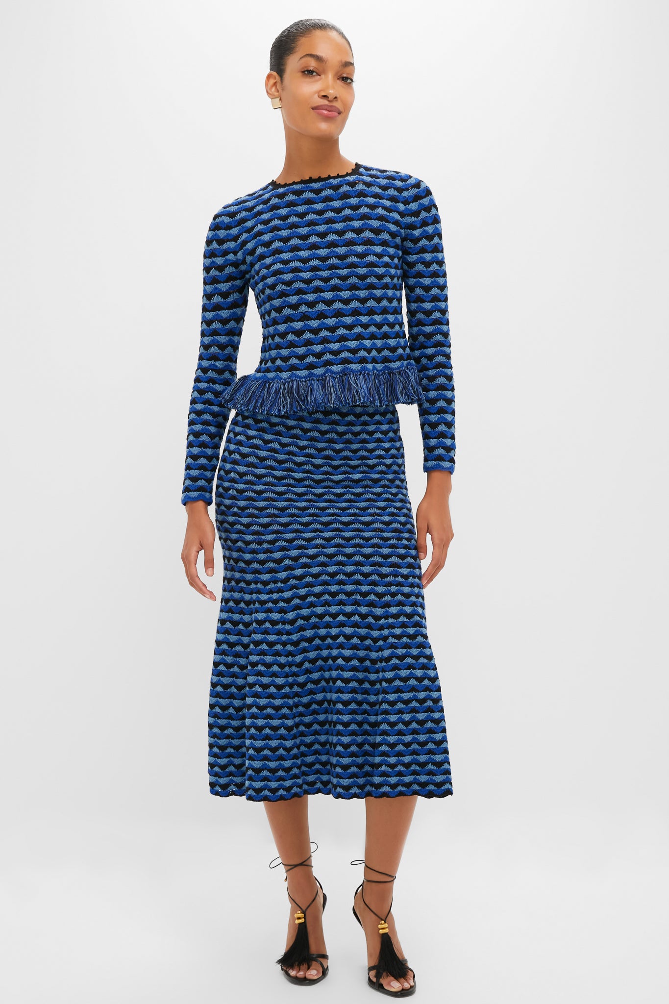 Woman models the classic Blue and Black Profundo Midi Skirt, featuring an effortless fit and flare silhouette with bold, wavy stripes and fun fringe detailing.