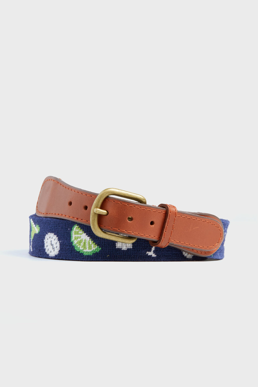 A navy needlepoint belt by Smathers and Branson with tan leather ends, a brass buckle, and hand-stitched designs of golf balls, lime wedges, and cocktail glasses.