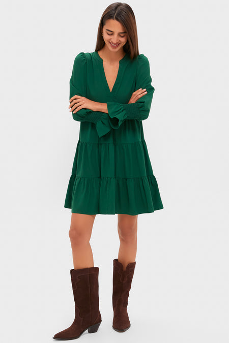 A woman stands with arms crossed, wearing a Pomander Place hunter green mini dress with tiered layers and dark brown mid-calf boots against a plain light background.