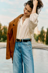 Woman in a white blouse, jeans, and a brown suede jacket. 