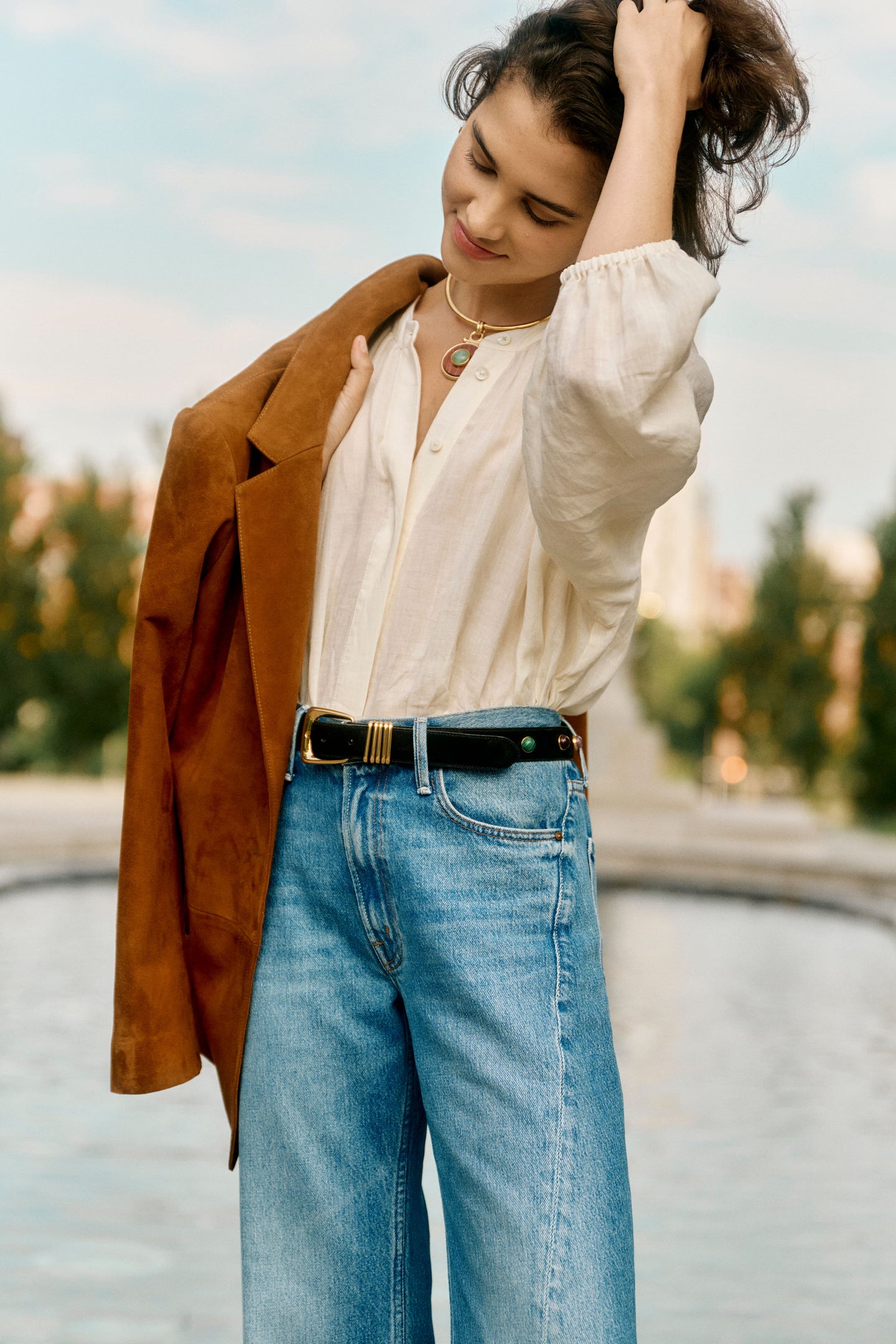 Woman in a white blouse, jeans, and a brown suede jacket. 