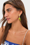 Woman wearing Multi Tesori Fish Charm Drop Earrings, featuring gold-tone seashell studs and playful green charms, paired with a classic blue and white patterned spaghetti-strap top.