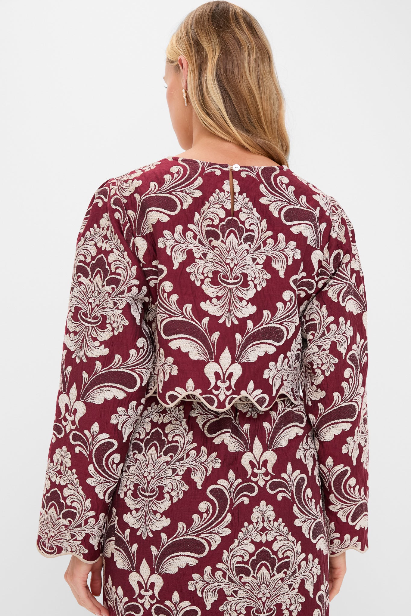Woman in Blush Pink and Burgundy Bicolor Jacquard Waves Long Sleeve Top, featuring classic baroque patterns and scalloped hem, embodies effortless, high-end style for fun, sophisticated occasions.