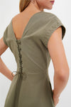A person wearing the Tuckernuck Burnt Olive Chino Solen Midi Dress, with a V-shaped back and corset-style closure, is shown from the back and side.