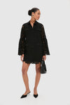 Model in classic Black Lace Long Sleeve Rachael Mini Dress with gold buttons, flared sleeves, and scalloped edges, paired with high-end mule heels and a chic handbag.