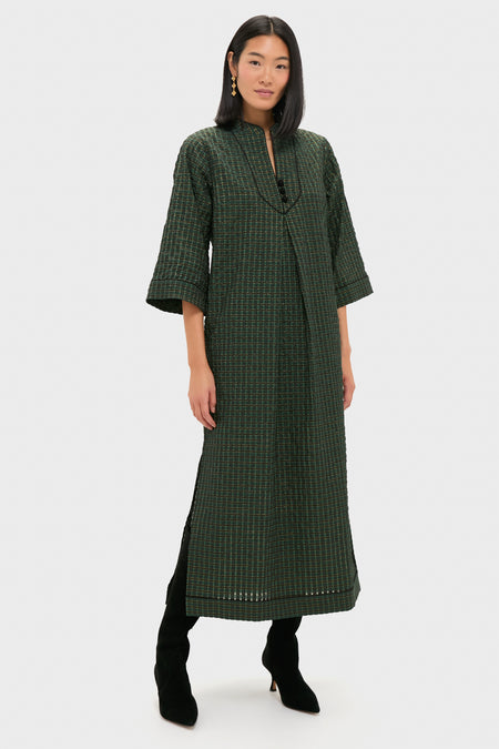 Woman in a classic, dark green Metallic Green Plaid Indy Maxi Dress, showcasing an effortless, high-end style with a relaxed fit and subtle shimmer, paired with black boots.