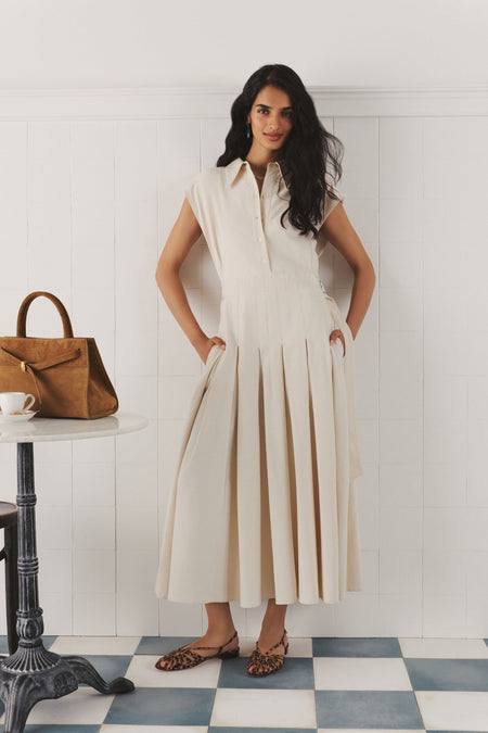 Woman in a cream maxi dress with a collar and a pleated skirt. 