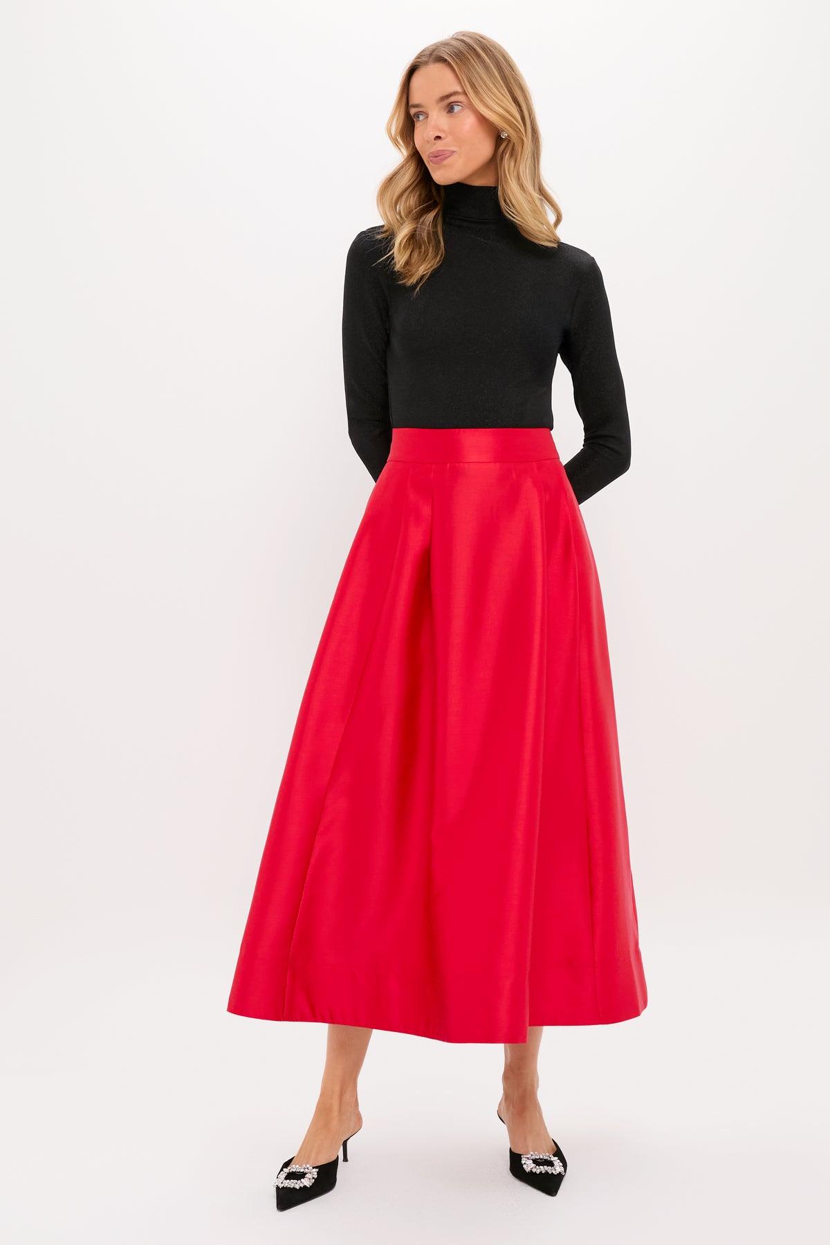 A woman in a Tuckernuck black turtleneck top, long bright red A-line skirt with elastic waistband, and black pointed-toe heels stands against a plain white background.
