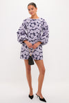 Woman in a Lilac & Navy Floral Jacquard Janie Mini Dress with balloon sleeves, holding a black pouch bag, wearing black pointed-toe mules, exuding classic, effortless style.