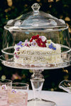Isabella Cake Stand elegantly displays a coconut-frosted cake under a glass cloche, embodying classic, effortless high-end style for a fun, garden-style gathering.
