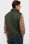 Man models Olive Winter Finn Gilet, a classic, high-end quilted vest with effortless style, featuring a high collar and practical pockets, embodying Tuckernuck's fun and confident spirit.