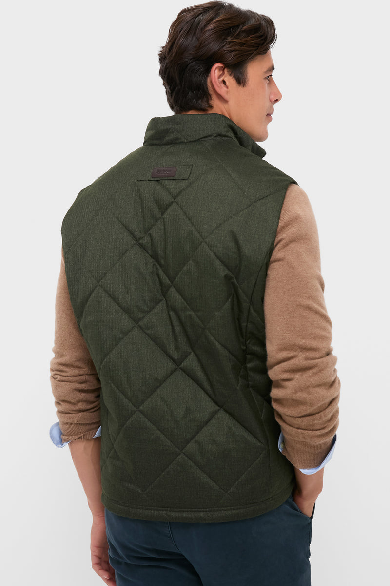 Man models Olive Winter Finn Gilet, a classic, high-end quilted vest with effortless style, featuring a high collar and practical pockets, embodying Tuckernuck's fun and confident spirit.