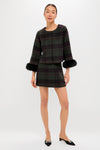 A woman wears a Tuckernuck dark plaid jacket with black fur cuffs and a matching wool mini skirt, styled with black pointed-toe flats—a chic transitional wardrobe piece.