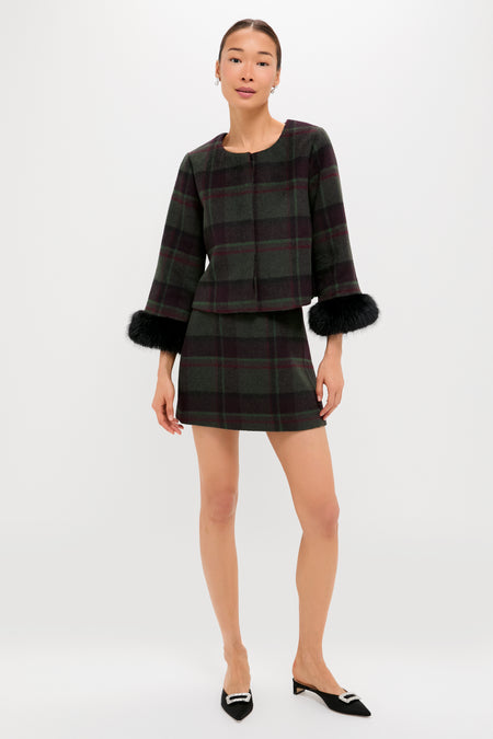 A woman wears a Tuckernuck dark plaid jacket with black fur cuffs and a matching wool mini skirt, styled with black pointed-toe flats—a chic transitional wardrobe piece.