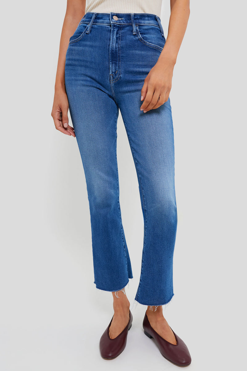 A person wears blue, high-waisted, slightly flared cropped jeans with raw hems from MOTHER, paired with brown flats.