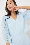 A woman poses in the Tuckernuck Airy Blue Daniella Top, featuring an eyelet floral design, scalloped edges, and three-quarter sleeves—a perfect summer blouse.