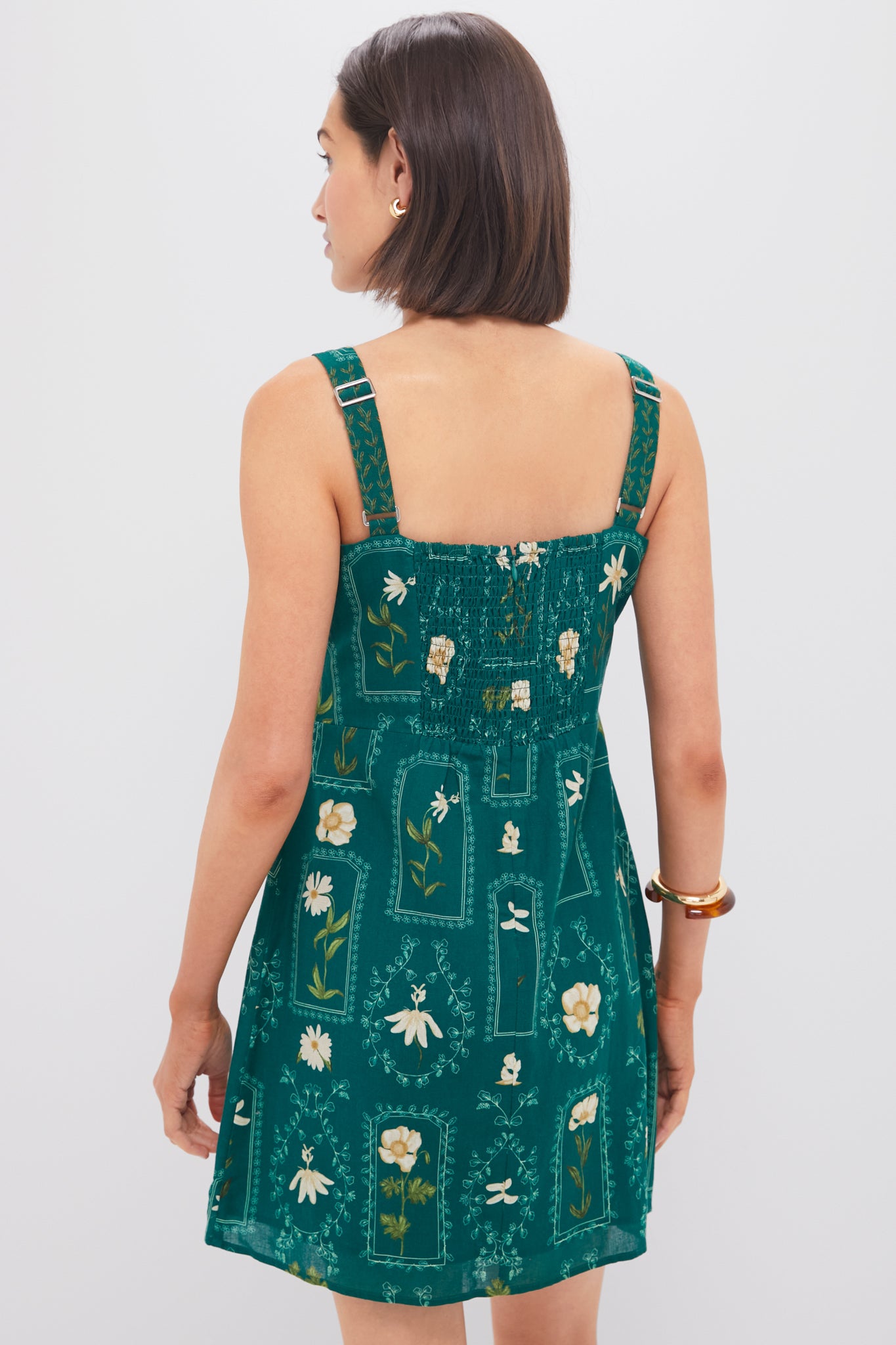 Woman in a deep green Teal Stem Merrit Mini Dress with adjustable straps and smocked back, embodying effortless, classic style for fun, high-end occasions.