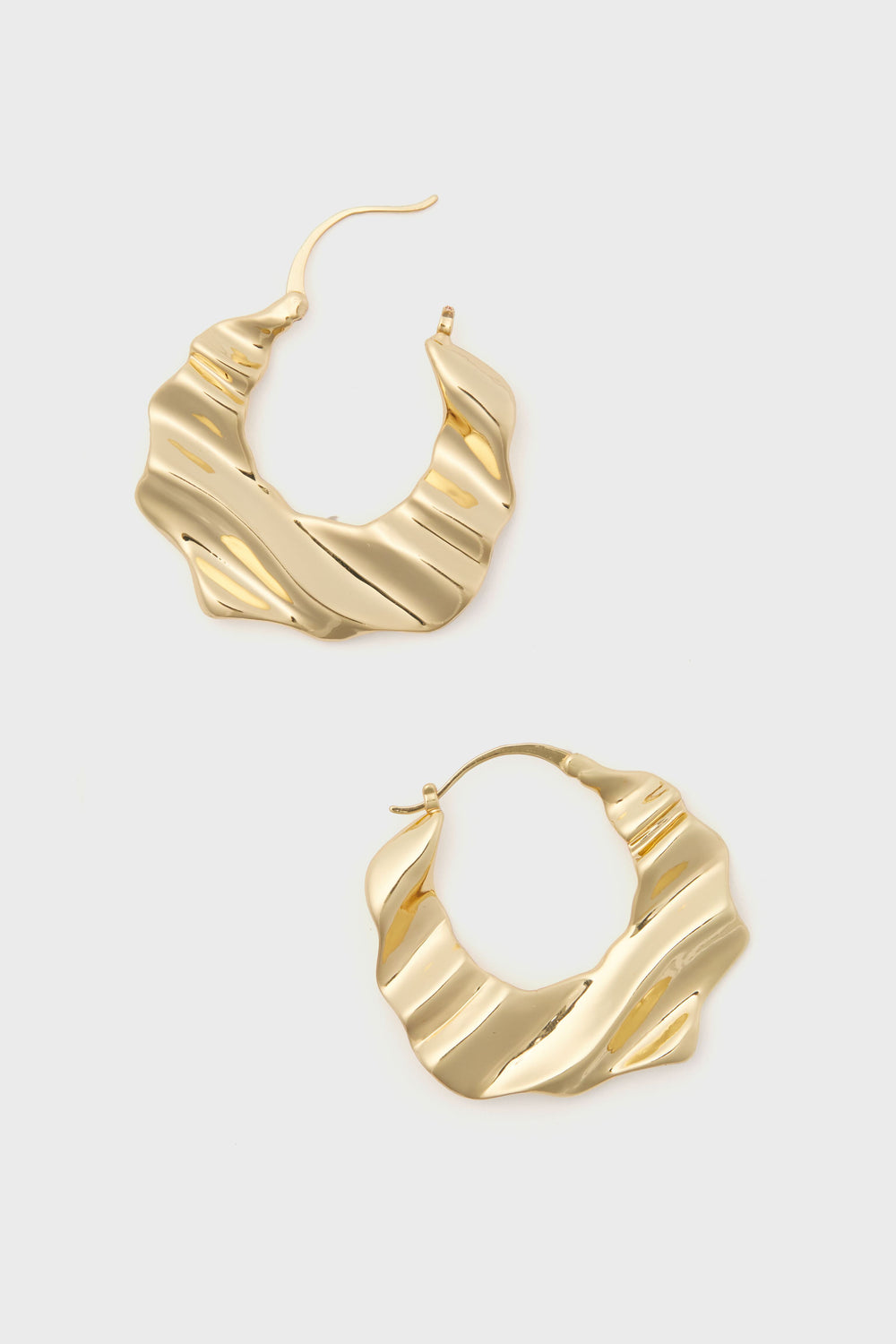 The Gold Nahla Earrings by Mignonne Gavigan are gold-tone, wavy textured statement hoops, crafted as 14k gold-plated jewelry.