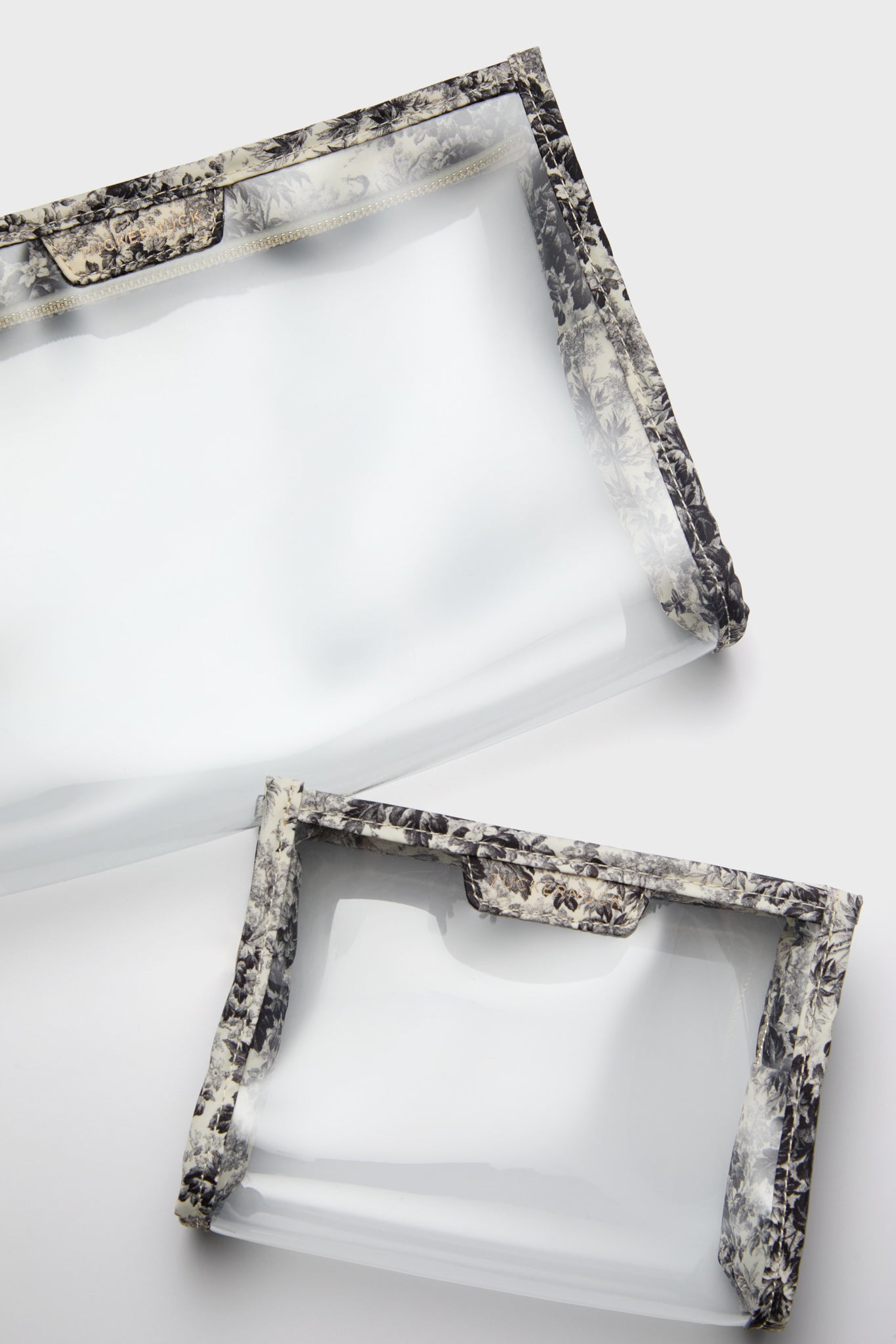 Two translucent rectangular pouches with a Noir Cypress Toile print trim.