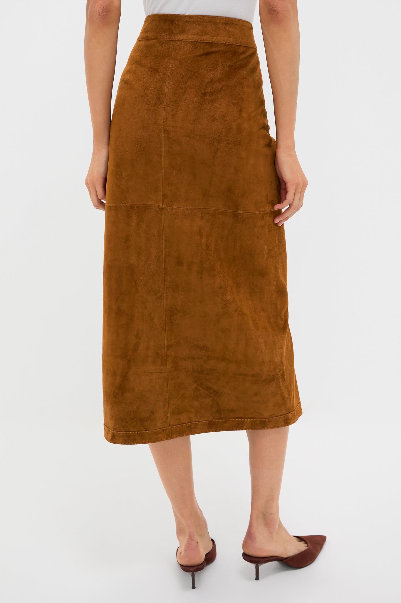Back view of a woman wearing the classic Nutmeg Winona Skirt, a high-end, effortless suede midi with a wrap design, paired with pointed-toe mules.