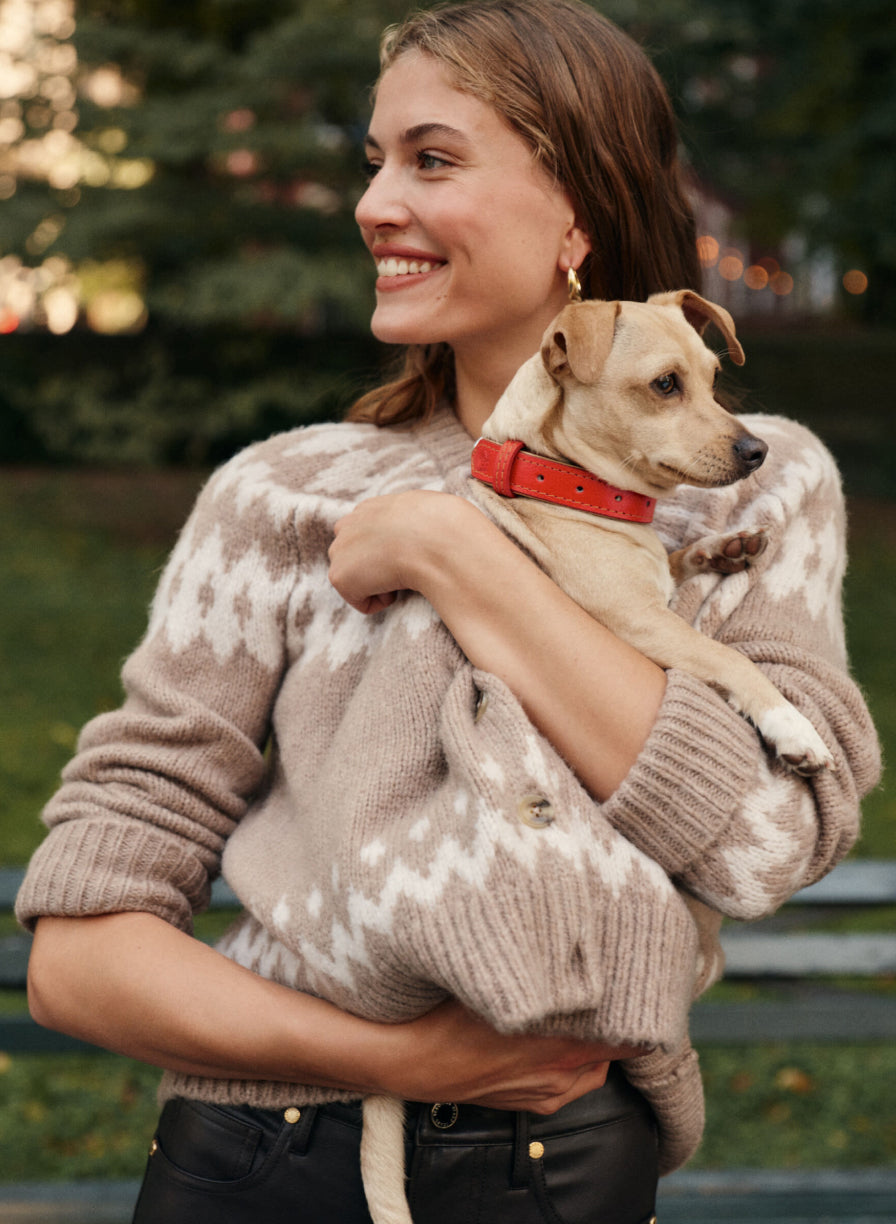 A woman holds a dog inside of her fair isle patterned cardigan.