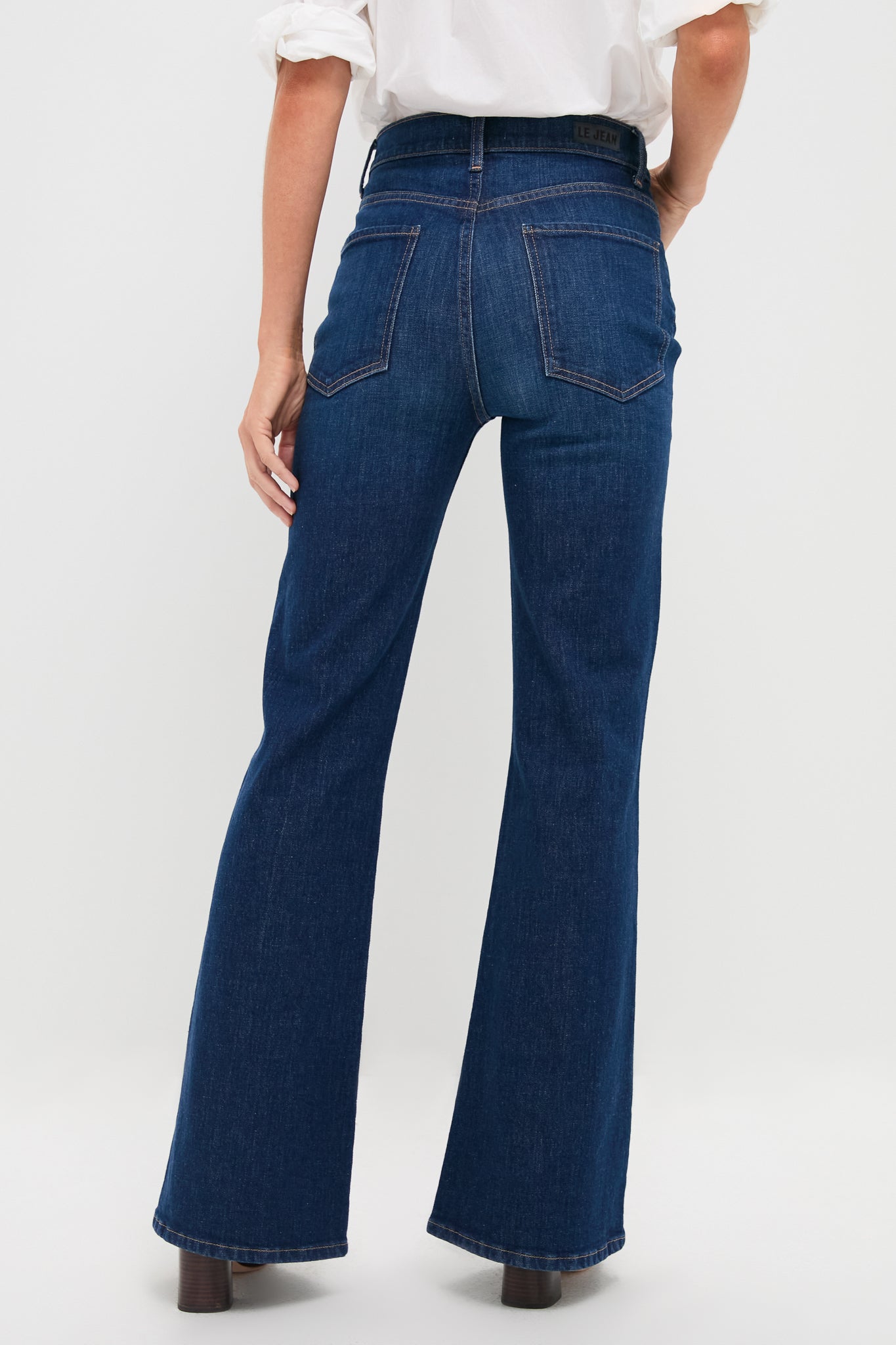 Woman in Zoe Gigi High Rise Skinny Flare jeans, showcasing a classic, effortless flared leg design paired with a tucked white shirt and ankle boots.