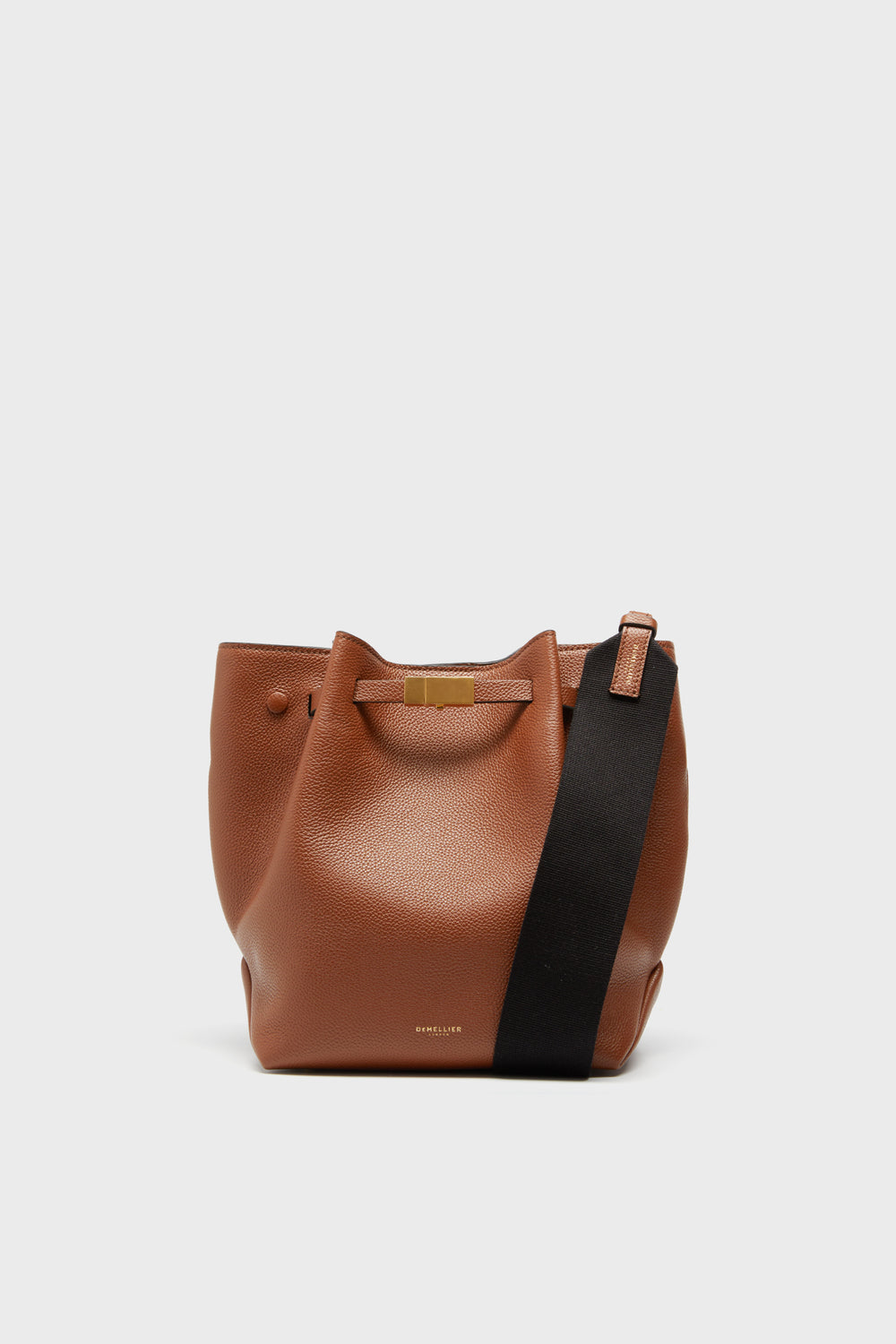 The Demellier brown leather bucket bag, made from Italian and Spanish materials, features a wide black shoulder strap and a gold-tone buckle.