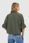 Rear view of person in olive-green Duffle Bag Next Ex Shirt, showcasing its classic, effortless style with a boxy silhouette and rolled sleeves, paired with jeans.