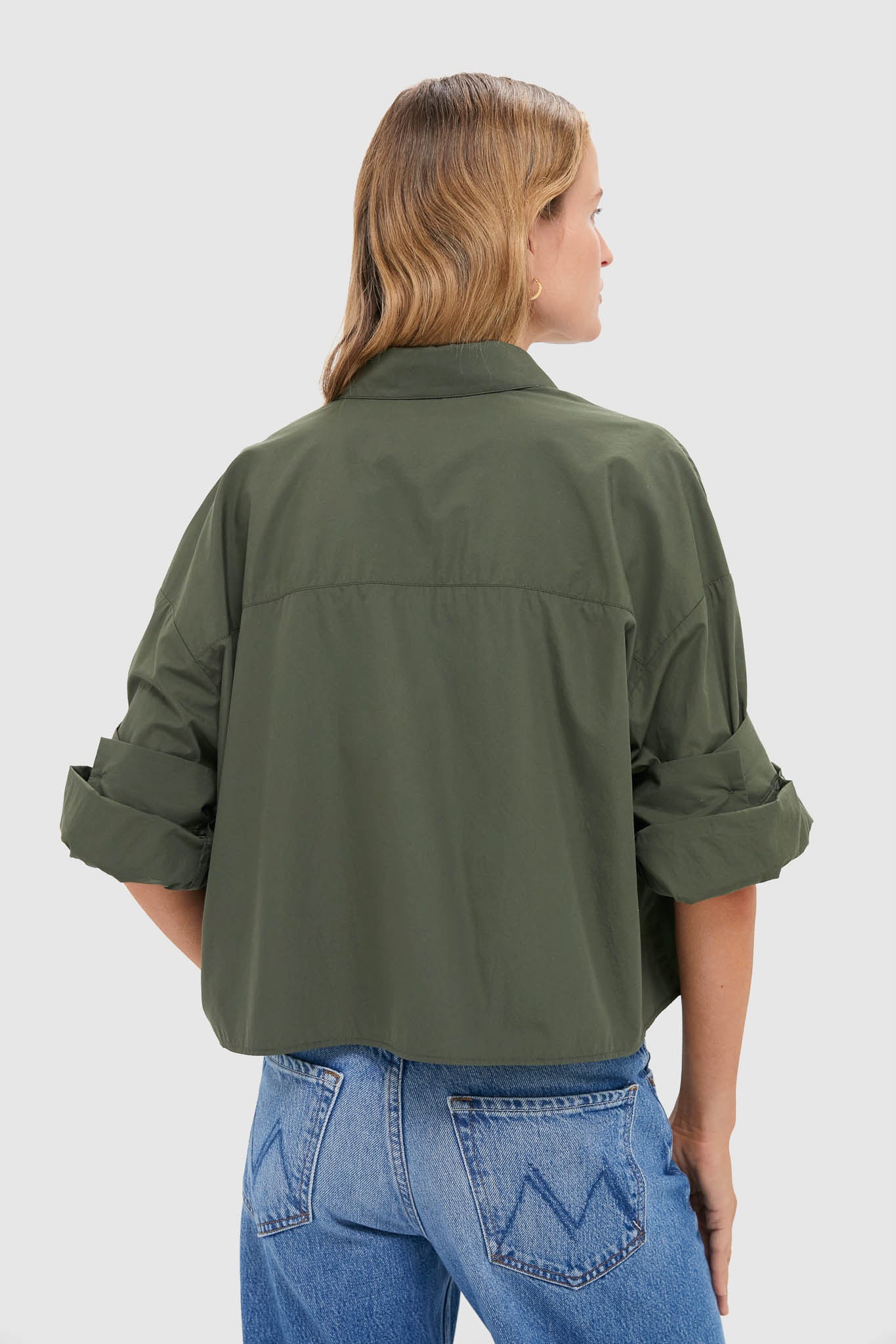 Rear view of person in olive-green Duffle Bag Next Ex Shirt, showcasing its classic, effortless style with a boxy silhouette and rolled sleeves, paired with jeans.