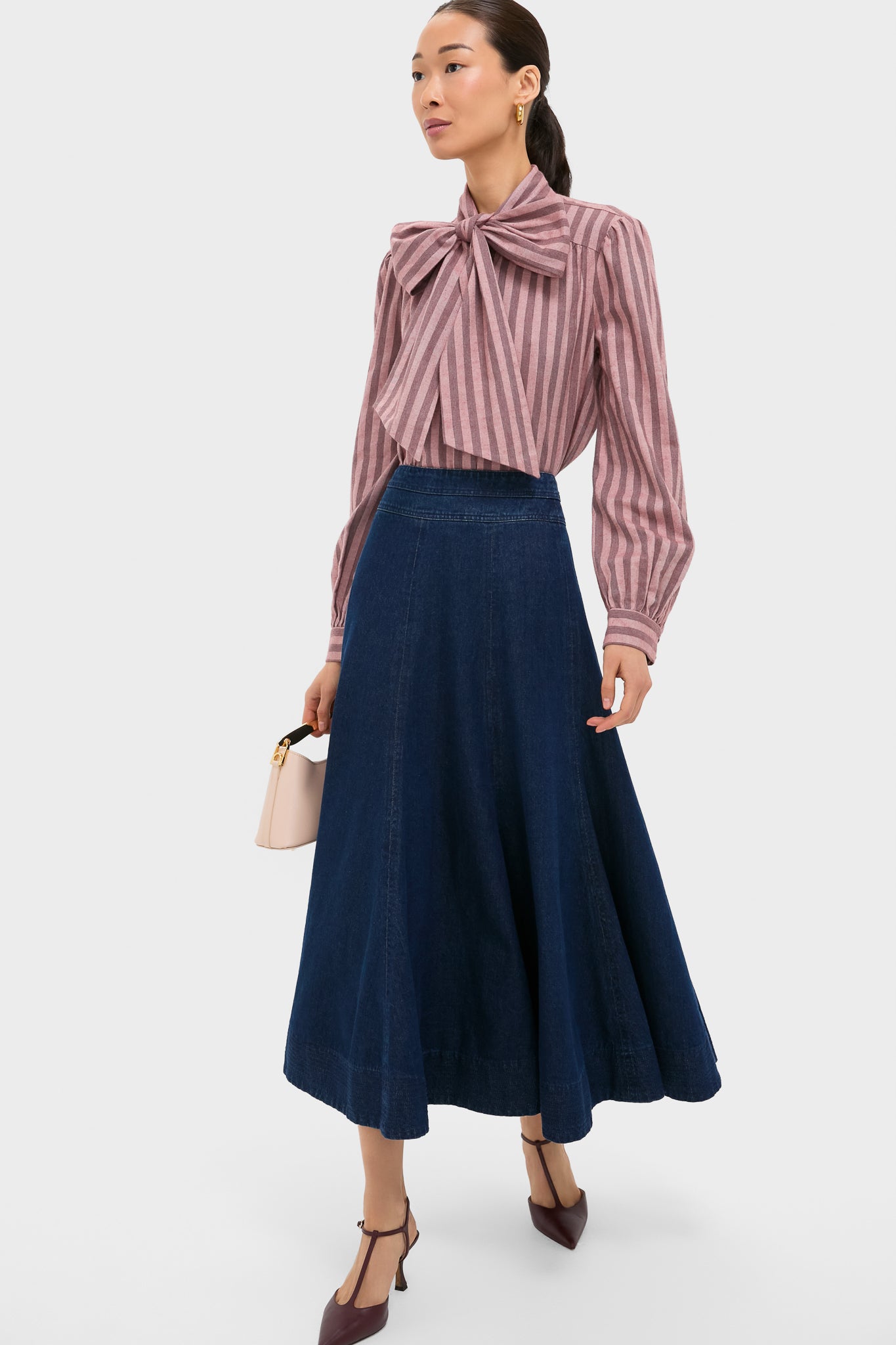 Model wearing the classic Mauve Stripe Brianna Bow Blouse with a dramatic bow, paired effortlessly with a high-end denim skirt and fun burgundy heels, showcasing an elegant, confident style.