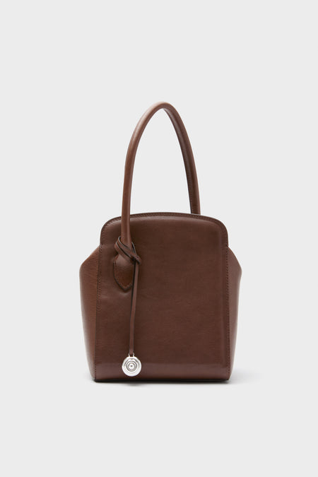 The Liffner brown calf leather purse features two handles and a silver circular charm, combining Scandinavian-inspired design with timeless elegance for any outfit.