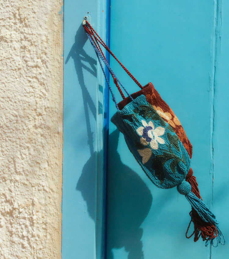 Two beaded bags, one blue and one brown, blowing in the wind from a post on a door. 