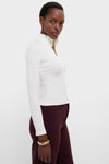 A person wearing a white long-sleeve, collared Citizens of Humanity Sheena Henley in ribbed cotton and burgundy pants stands against a plain white background.
