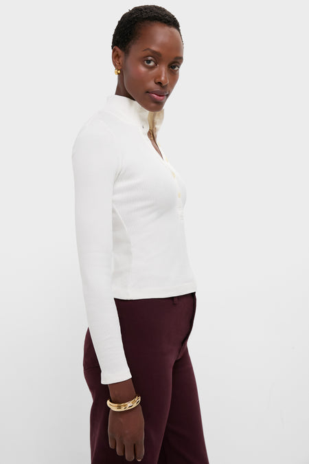 A person wearing a white long-sleeve, collared Citizens of Humanity Sheena Henley in ribbed cotton and burgundy pants stands against a plain white background.