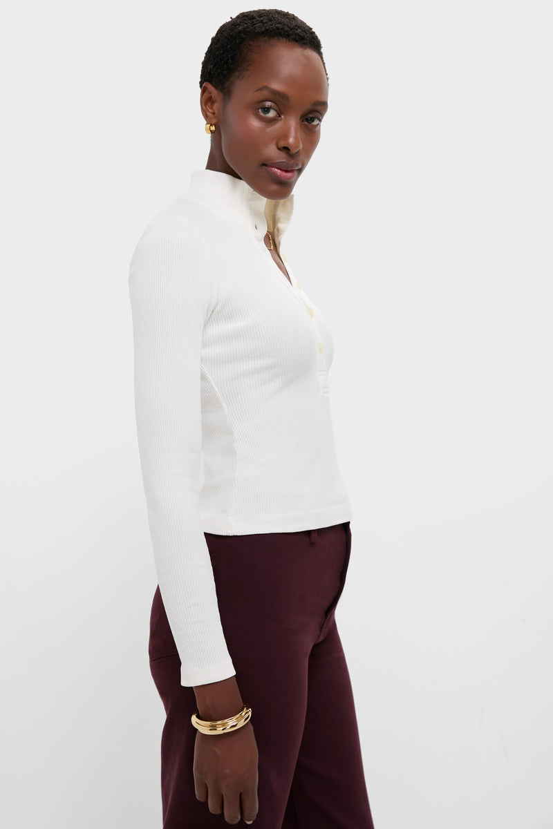 A person wearing a white long-sleeve, collared Citizens of Humanity Sheena Henley in ribbed cotton and burgundy pants stands against a plain white background.