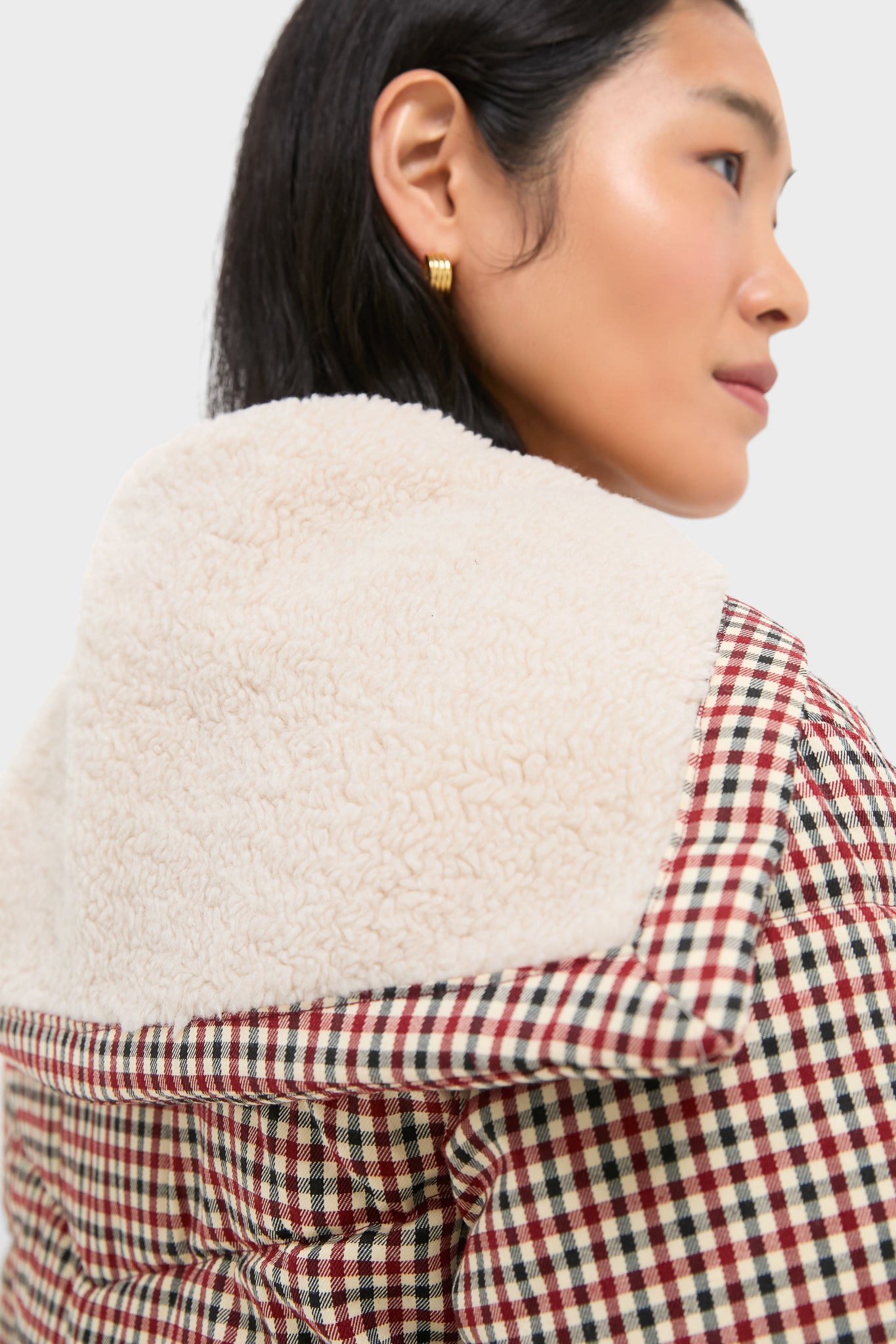 A person wears a gold hoop earring and a checked jacket with a large cream shearling collar by Greylin—standout, stylish outerwear thats perfect for cold weather.