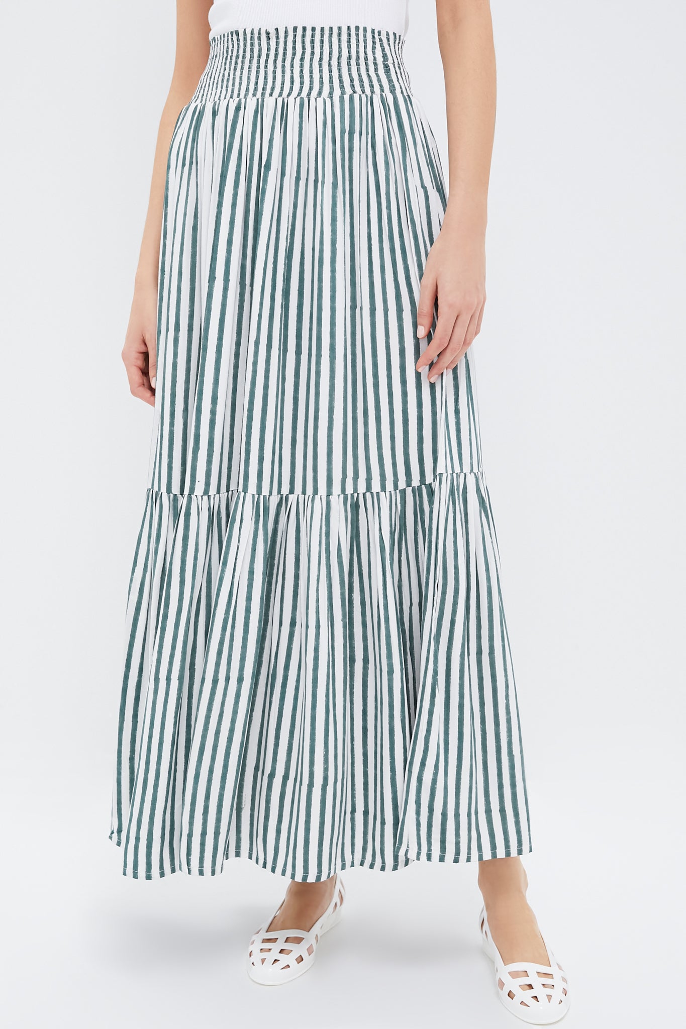 Person wearing a Love Tomas by Emerson Fry white and green vertically striped tiered maxi skirt, paired with a white sleeveless top and white cut-out flat shoes.