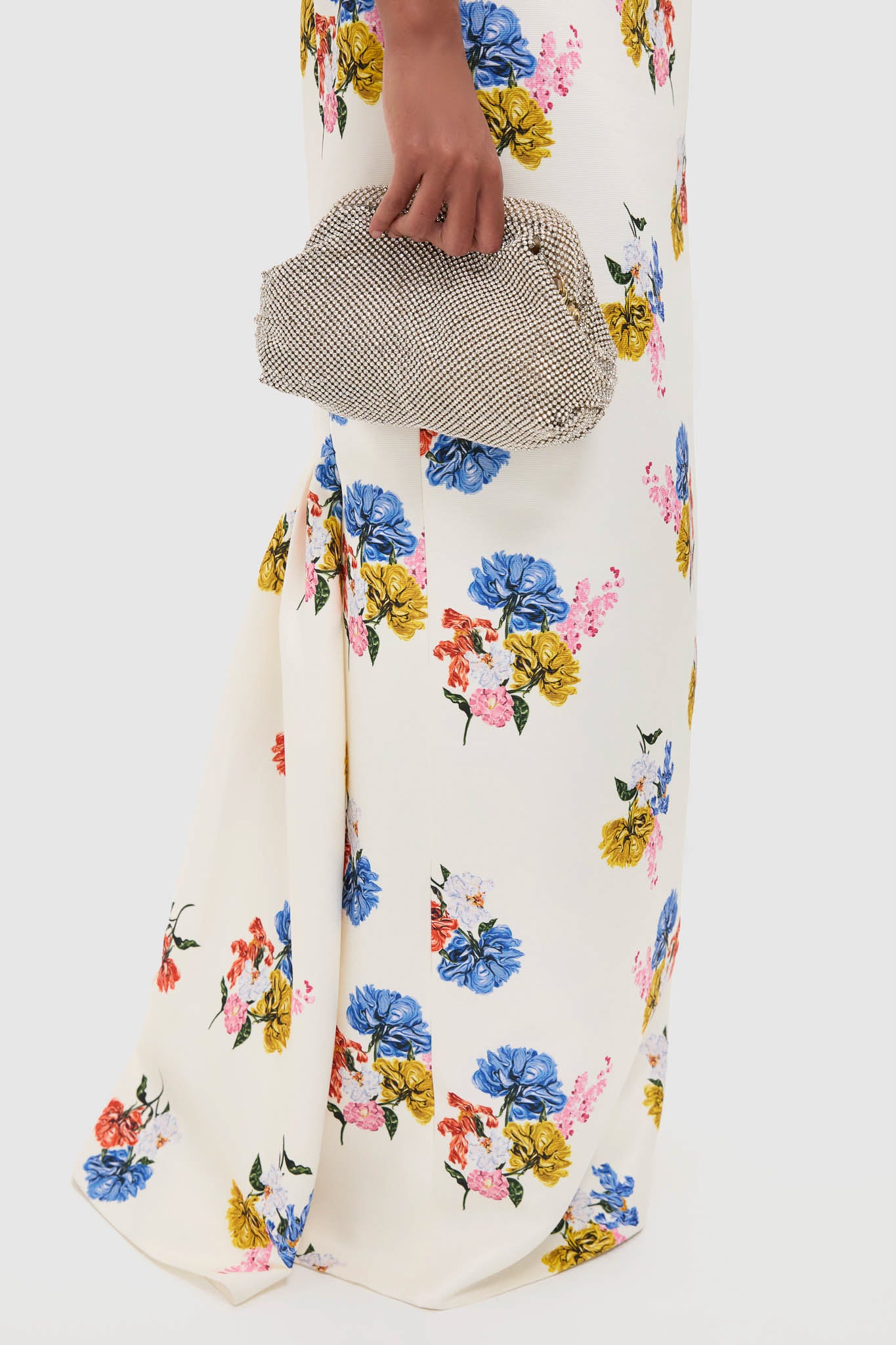 Woman in Retro Bouquet on White Fosette Gown, a classic, floor-length dress with a floral motif, styled with an effortless, high-end silver evening clutch.