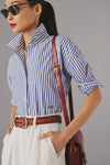 Woman in a blue and white striped button down shirt, with monogramming detail on the waist with scripted letters "SRV". 