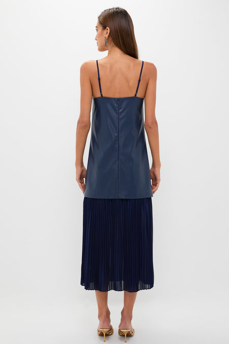 Woman in classic Mixed Media Leather Pleated Ozzy Midi Dress, featuring an effortless leather bodice and fun pleated skirt, styled with gold mule sandals and drop earrings.