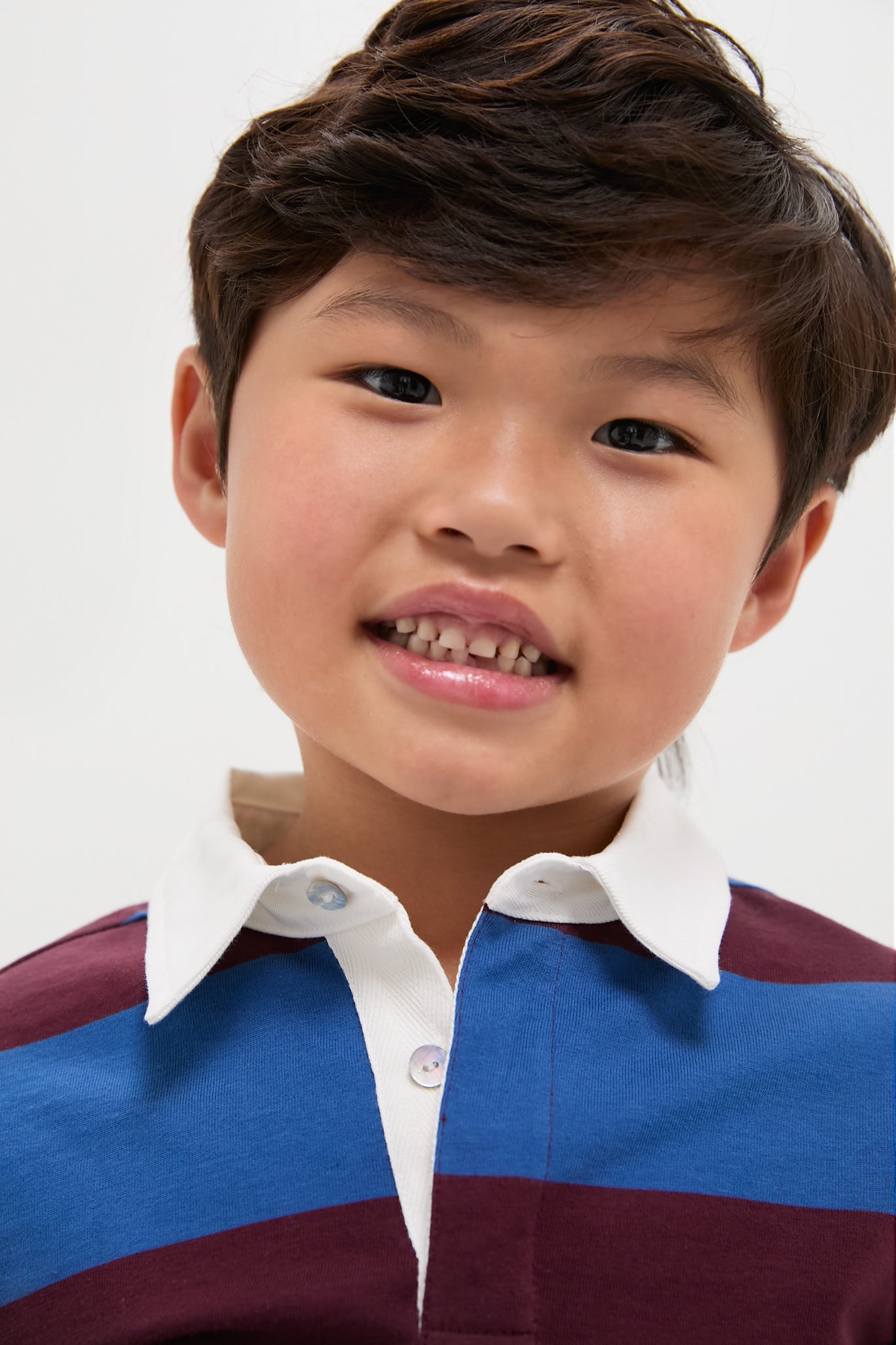 Young child wearing the Petrol Blue Stripe Tijo Long Sleeve Boy Rugby Shirt, showcasing a classic, effortless style with broad stripes and a white collar, exuding fun and high-end charm.