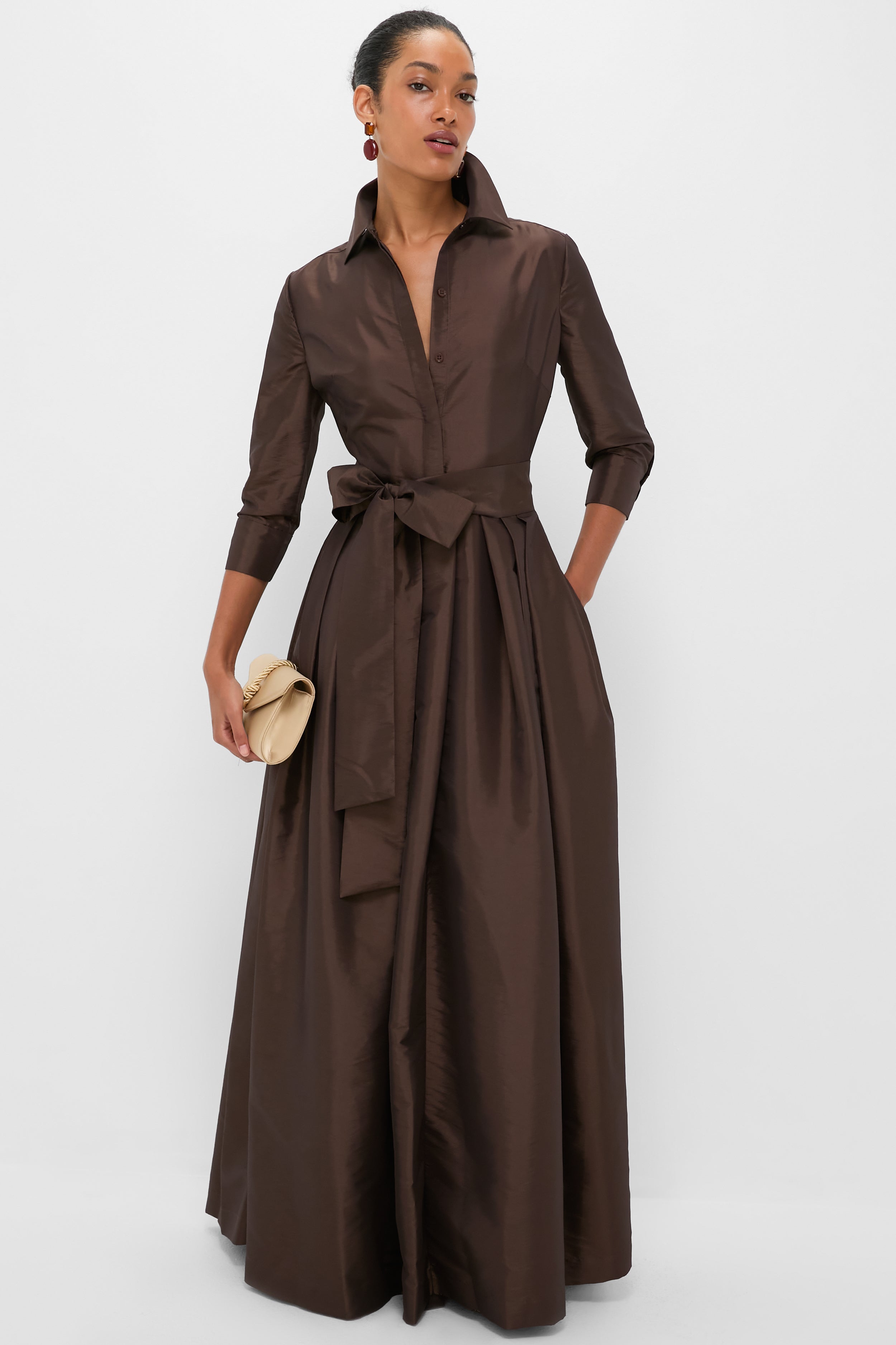 Woman in long brown shirtdress, holding soft-cream clutch, wears classic, high-end Carnelian Xiomara Earrings, adding an effortless touch of fun elegance.