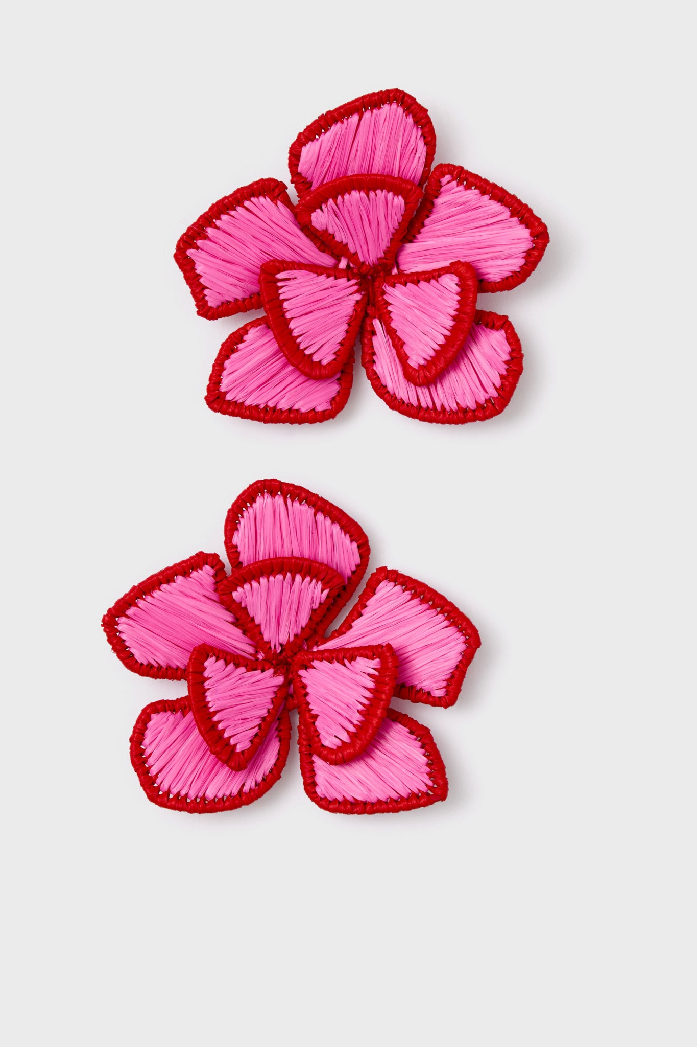 A pair of embroidered flower, applique earrings with pink petals outlined in red trim.
