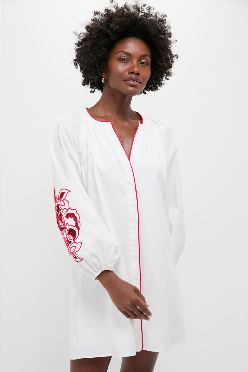 A woman wears the Hyacinth House White & Red Embroidery Steph Mini Dress, a cotton poplin piece with long balloon sleeves, red trim, and red floral embroidery on one sleeve for an elegant touch.