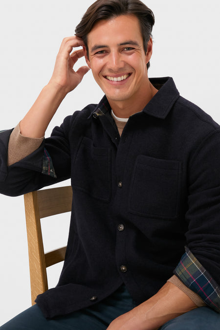 Young man models the Navy Marl Marlow Tailored Wool Blend Overshirt, showcasing its classic, effortless design with plaid-lined sleeves and chest pockets, embodying high-end, fun style.